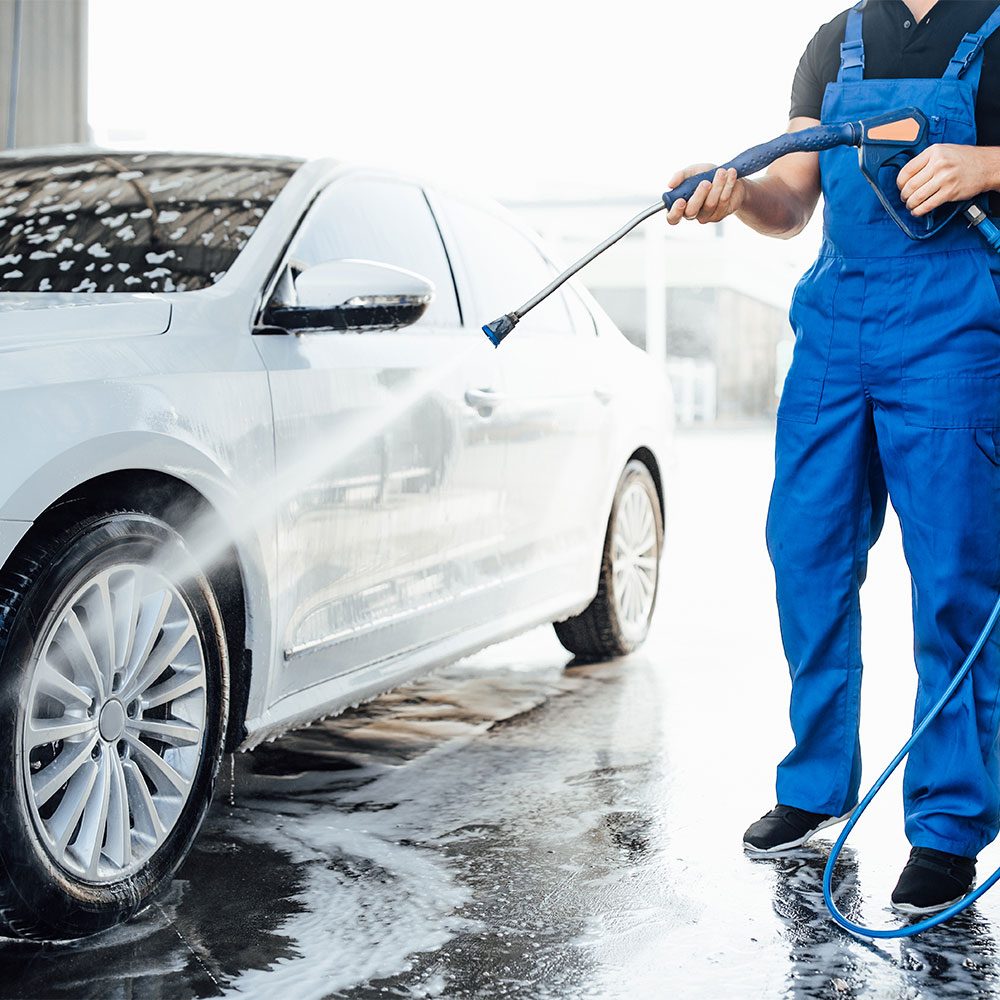 professional-washer-blue-uniform-washing-luxury-car-with-water-gun-open-air-car-wash